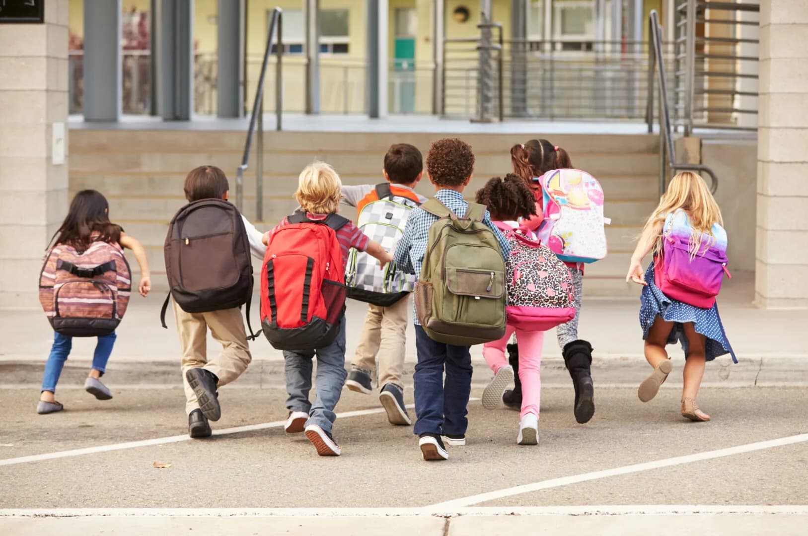 Elementary school kids running into school, back view